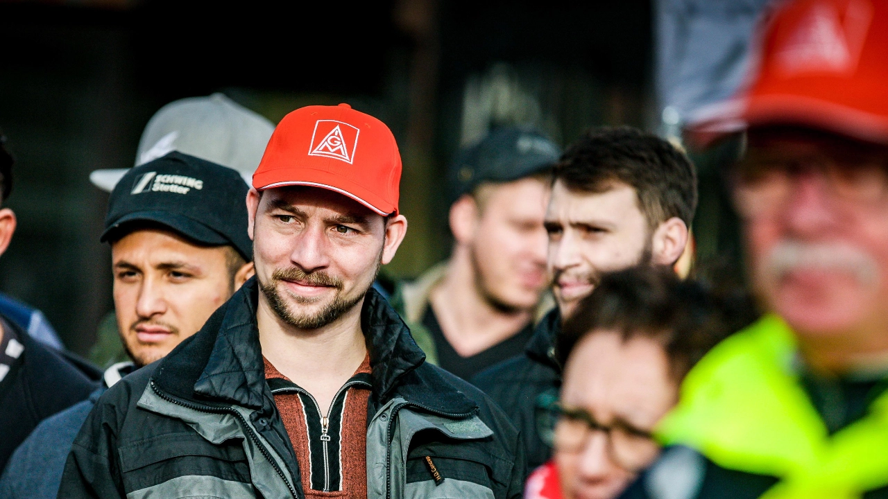 Ein junger Mann mit IG Metall-Kappe steht in eine Gruppe Menschen und lächelt.